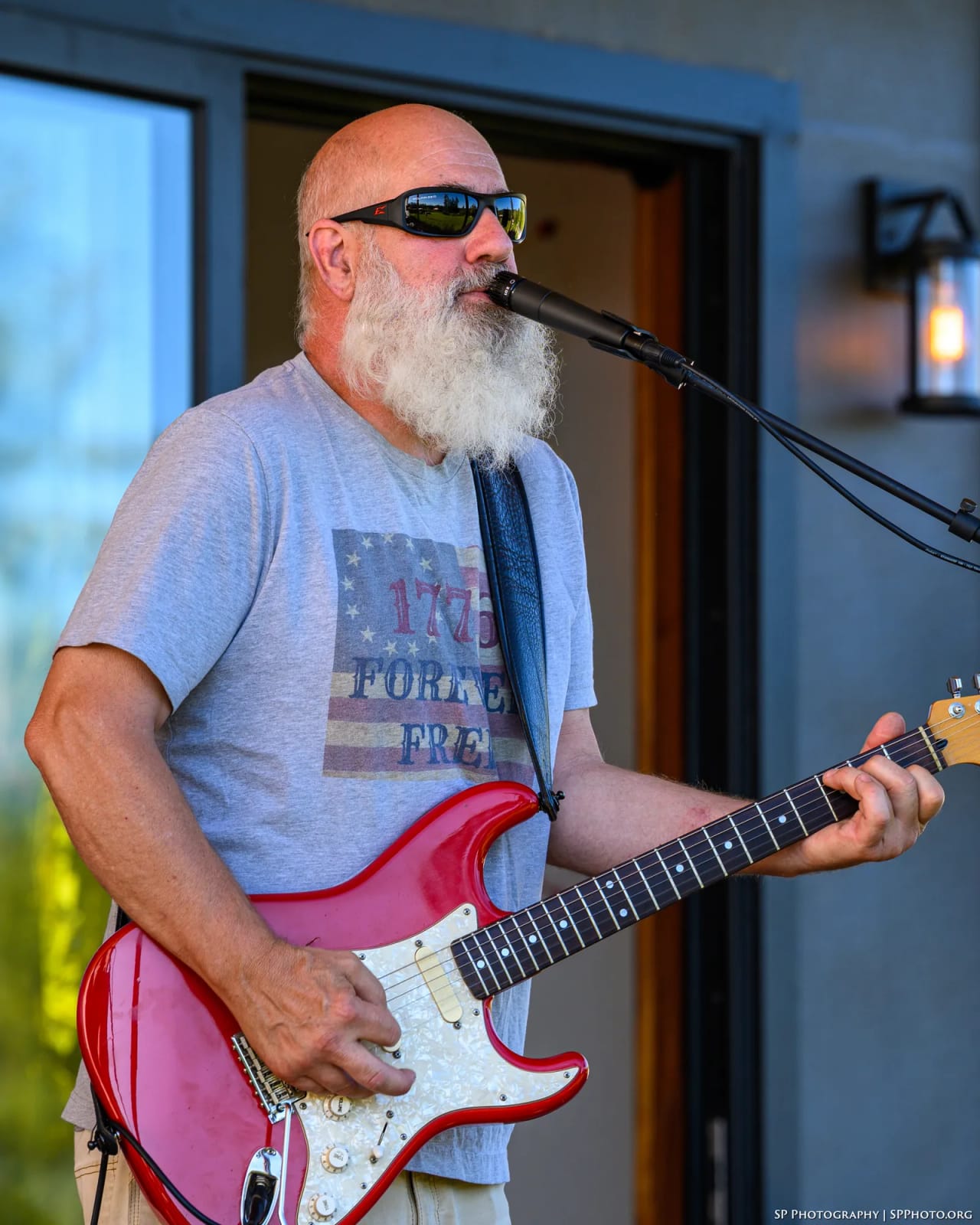 Carey Calhoun singing into the mic with his red Stratocaster, on an outdoor stage at dusk