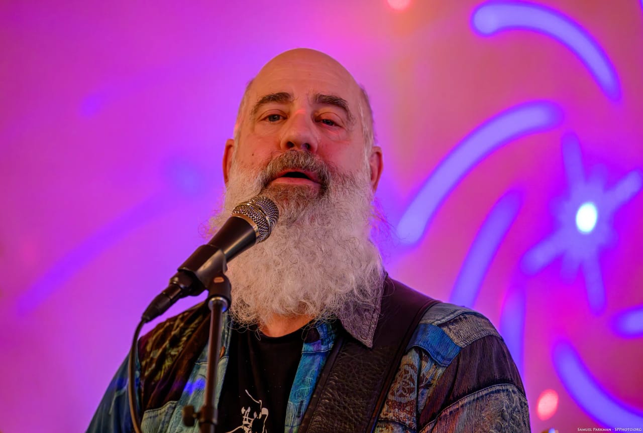 Carey Calhoun singing straight out at the room, purple and blue light patterns projected behind him