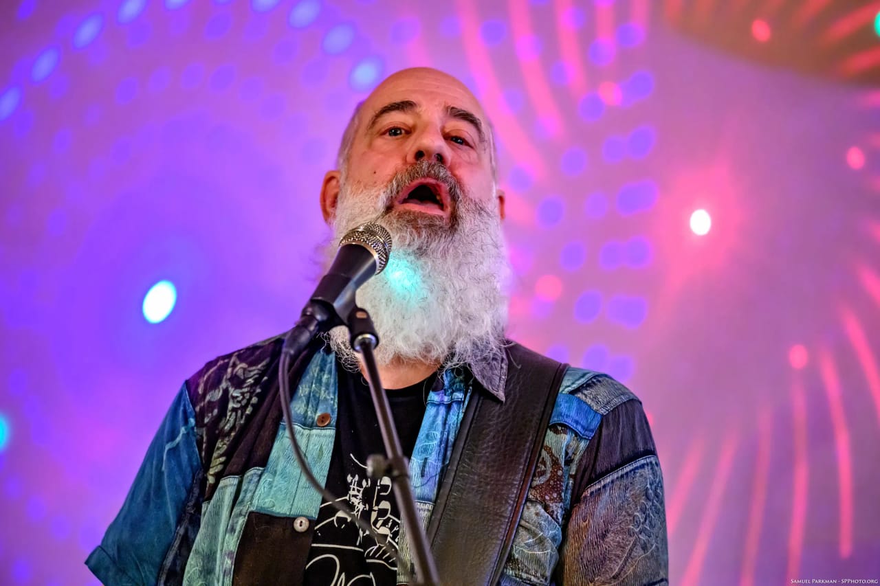 Carey Calhoun singing with his head tilted back at the mic, purple stage lights washing the wall behind him