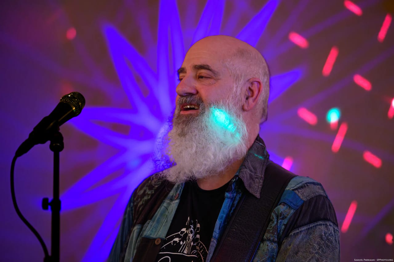Carey Calhoun grinning mid-song, a blue starburst projected on the wall behind him