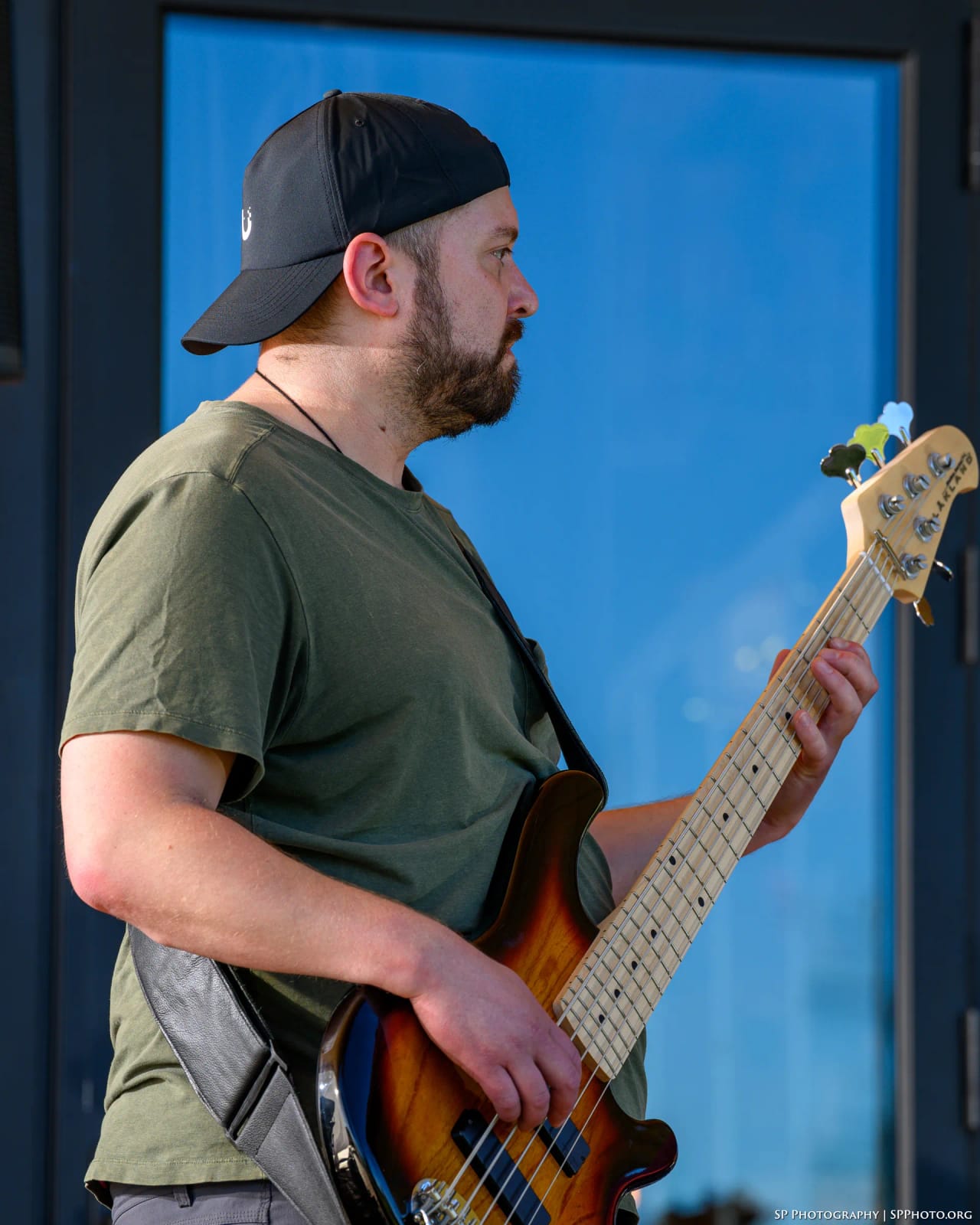 Grant Stampfli in profile with his sunburst five-string bass, blue glass behind him