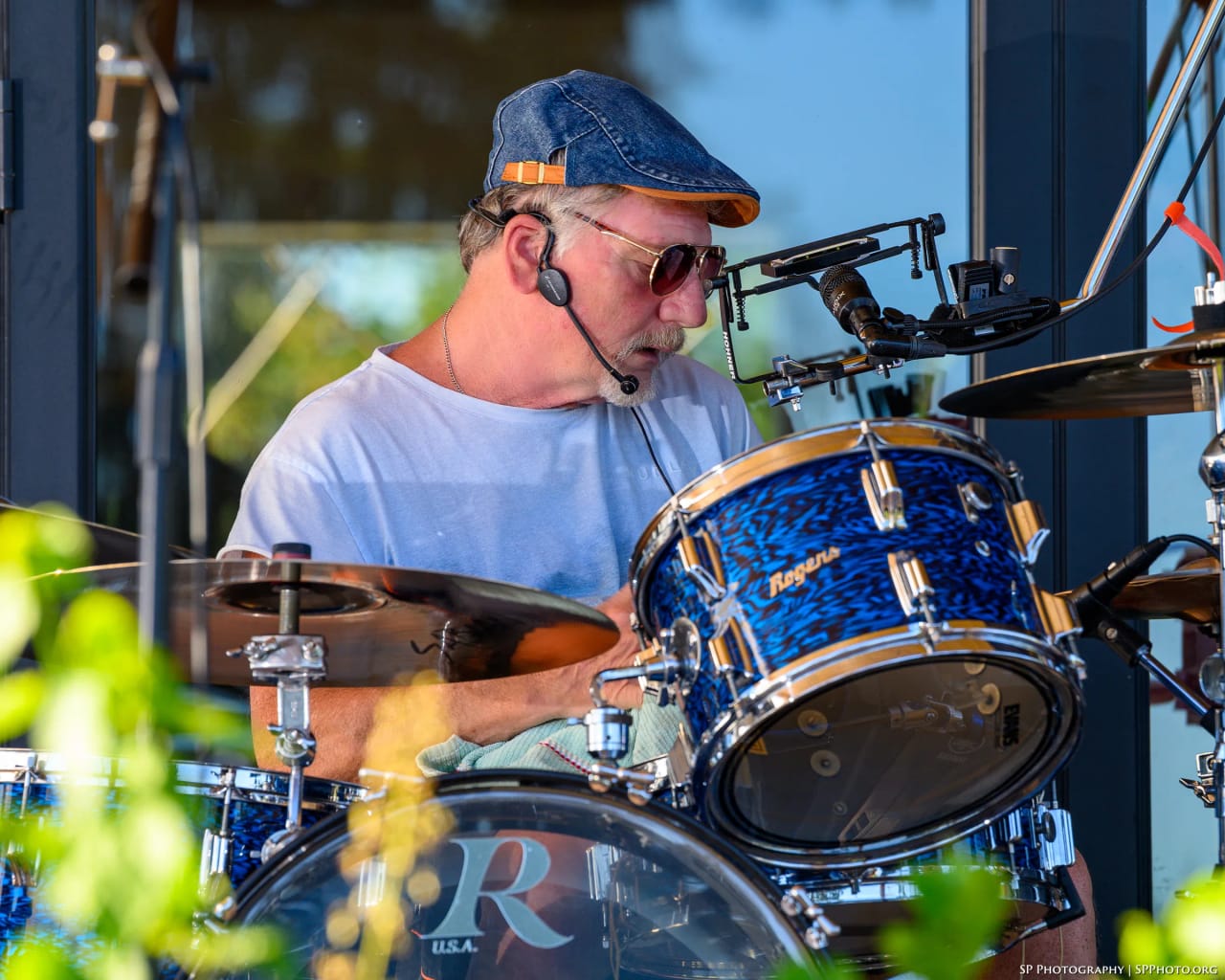 Mike Lynch at the blue Rogers kit in low evening sun, mic boom over the snare